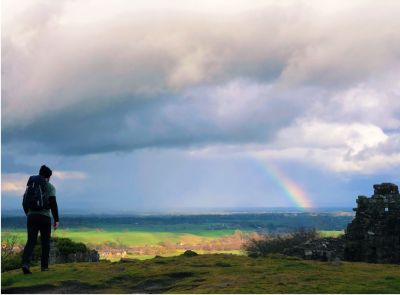Hiker walking on a hill with a rainbow across the sky